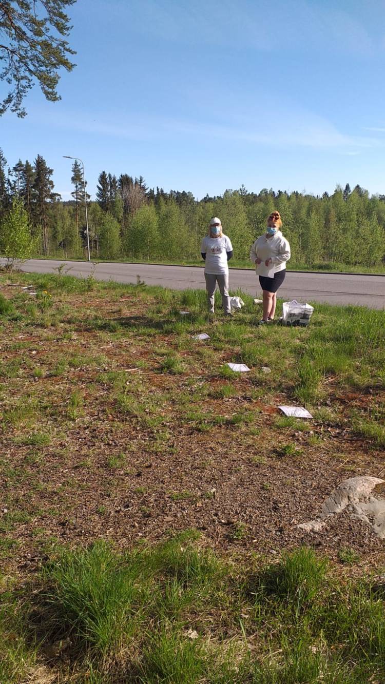 Kaksi lähihoitajaopiskelijaa seisoo tien reunassa. Maassa on valkoisia tehtäväpapereita.