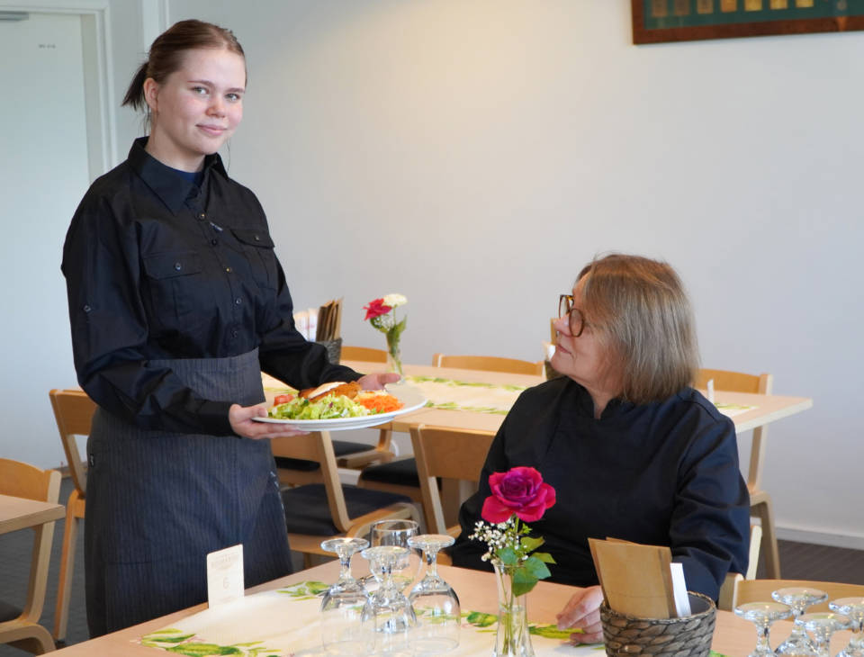 Henkilö tarjoilemassa ruoka-annosta toiselle henkilölle.