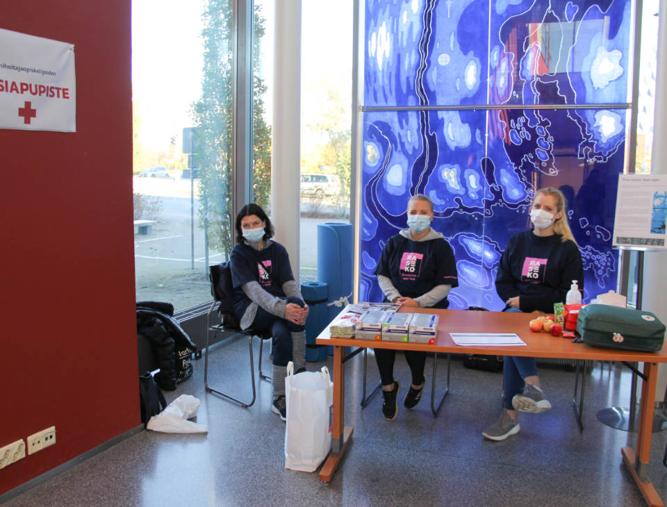 Kolme lähihoitajaopiskelijaa istuvat pöydän ääressä kirjaston aulassa.