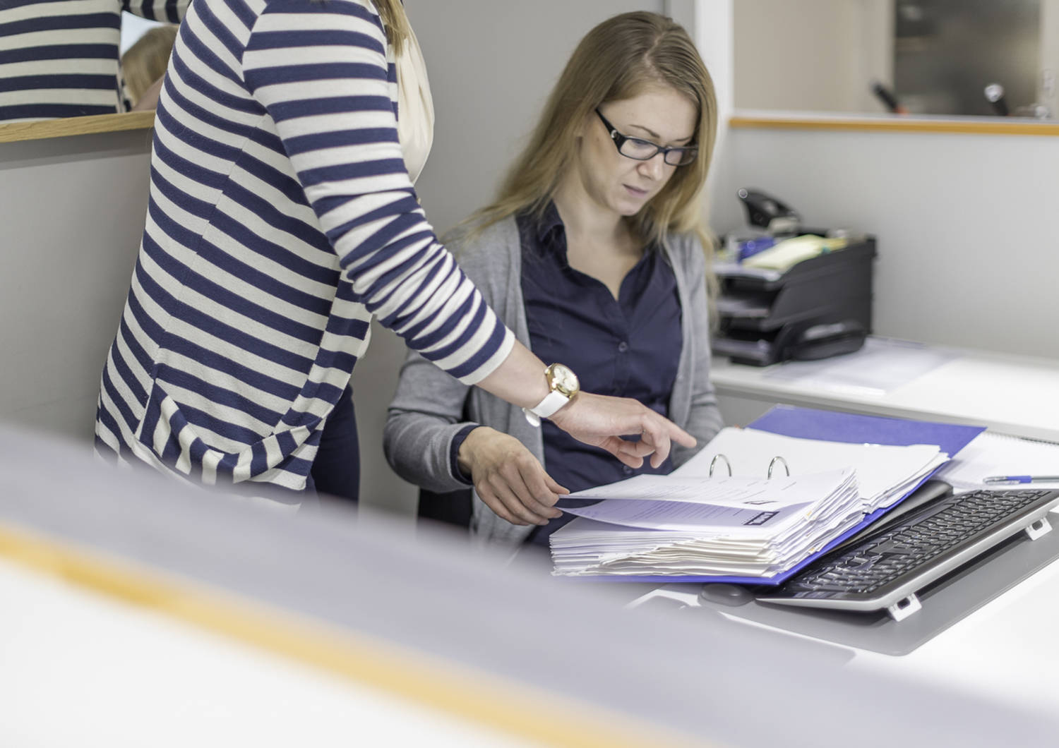 Tilitoimiston työntekijä käy läpi kansiossa olevia papereita kollegan kanssa.