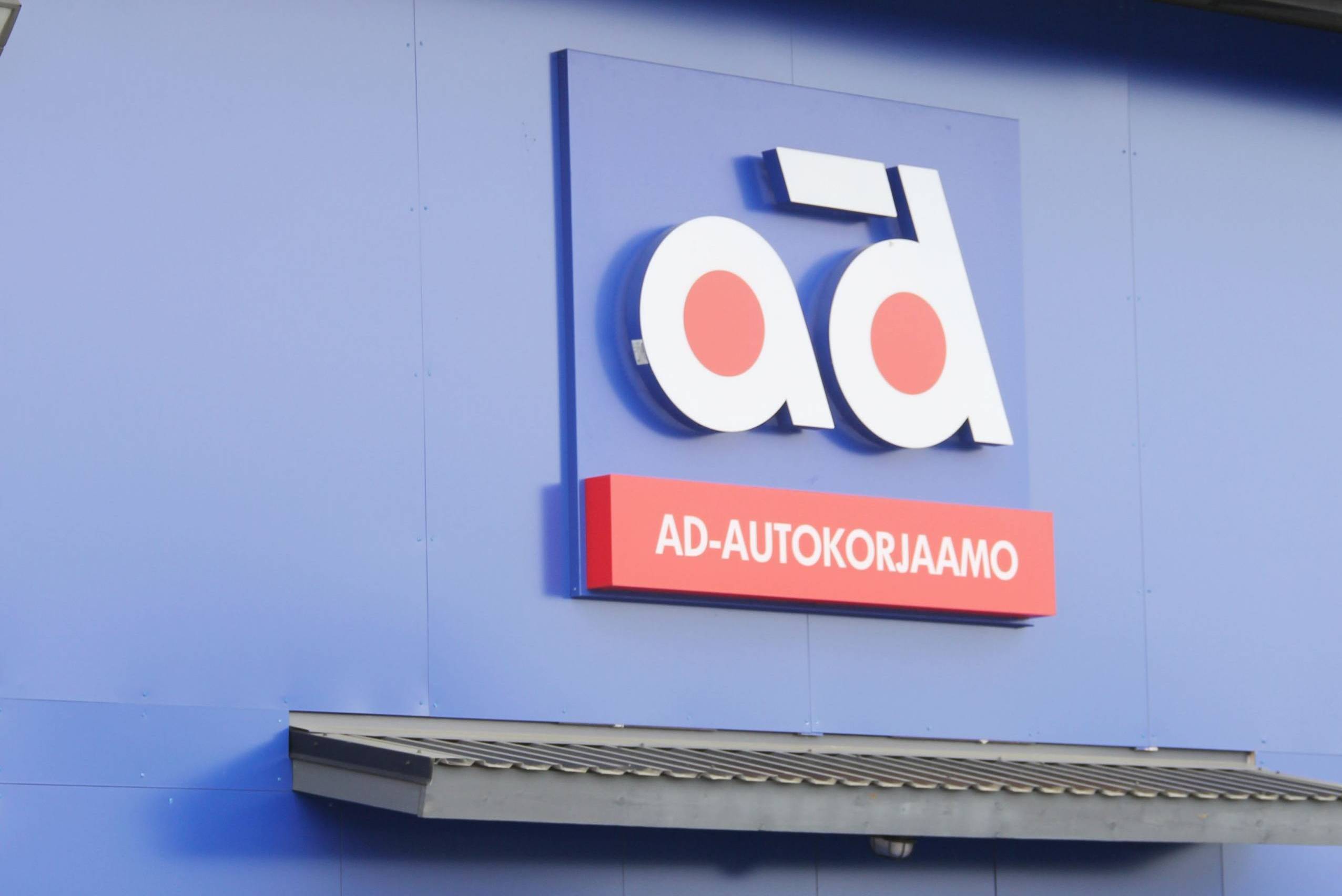 AD-Autokorjaamon logo sinisellä korjaamorakennuksen seinällä.