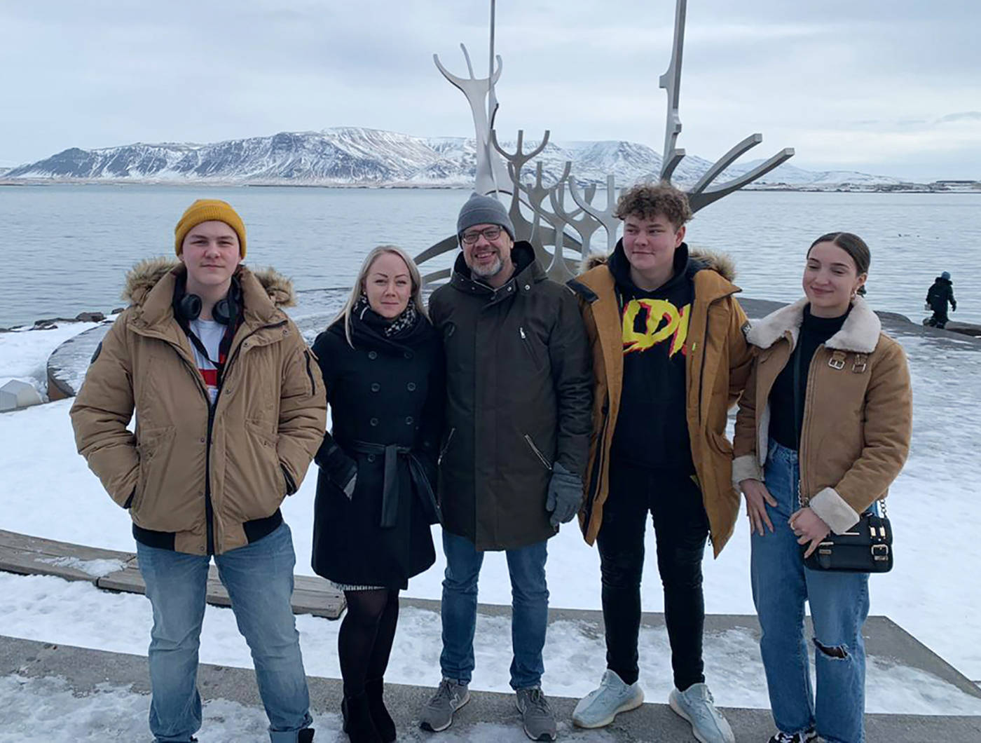 Viisi henkilöä seisoo rivissä ulkona. Taustalla näkyy maisema Islannista.