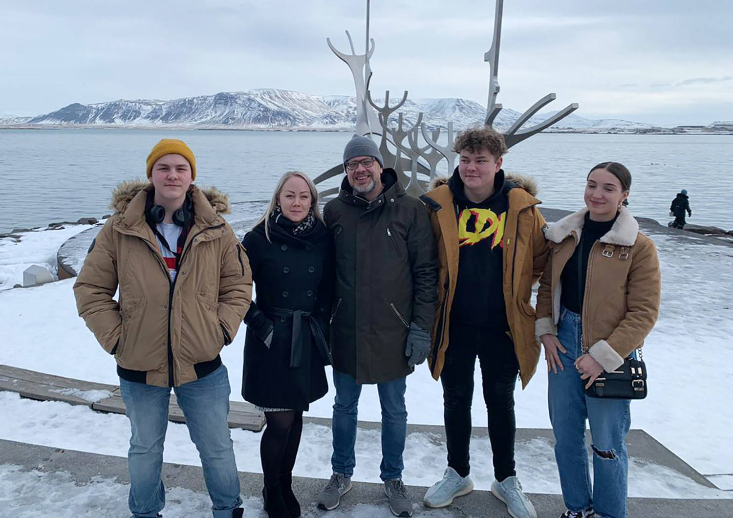 Viisi henkilöä seisoo rivissä ulkona. Taustalla näkyy maisema Islannista.