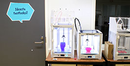 Kaksi 3D printteriä, joissa on muoviset kipot sisällä. Seinällä teksti "Ideasta tuotteeksi".