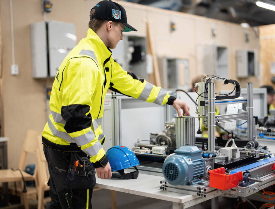 Huomiotyövaatteisiin pukeutunut nuori automaatiolinjan ääressä.