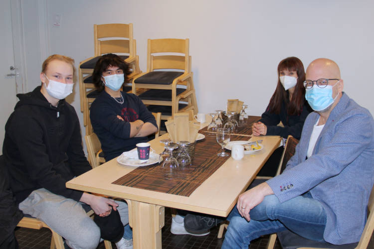 Neljä henkilöä maskit kasvoillaan ravintolapöydän ympärillä.