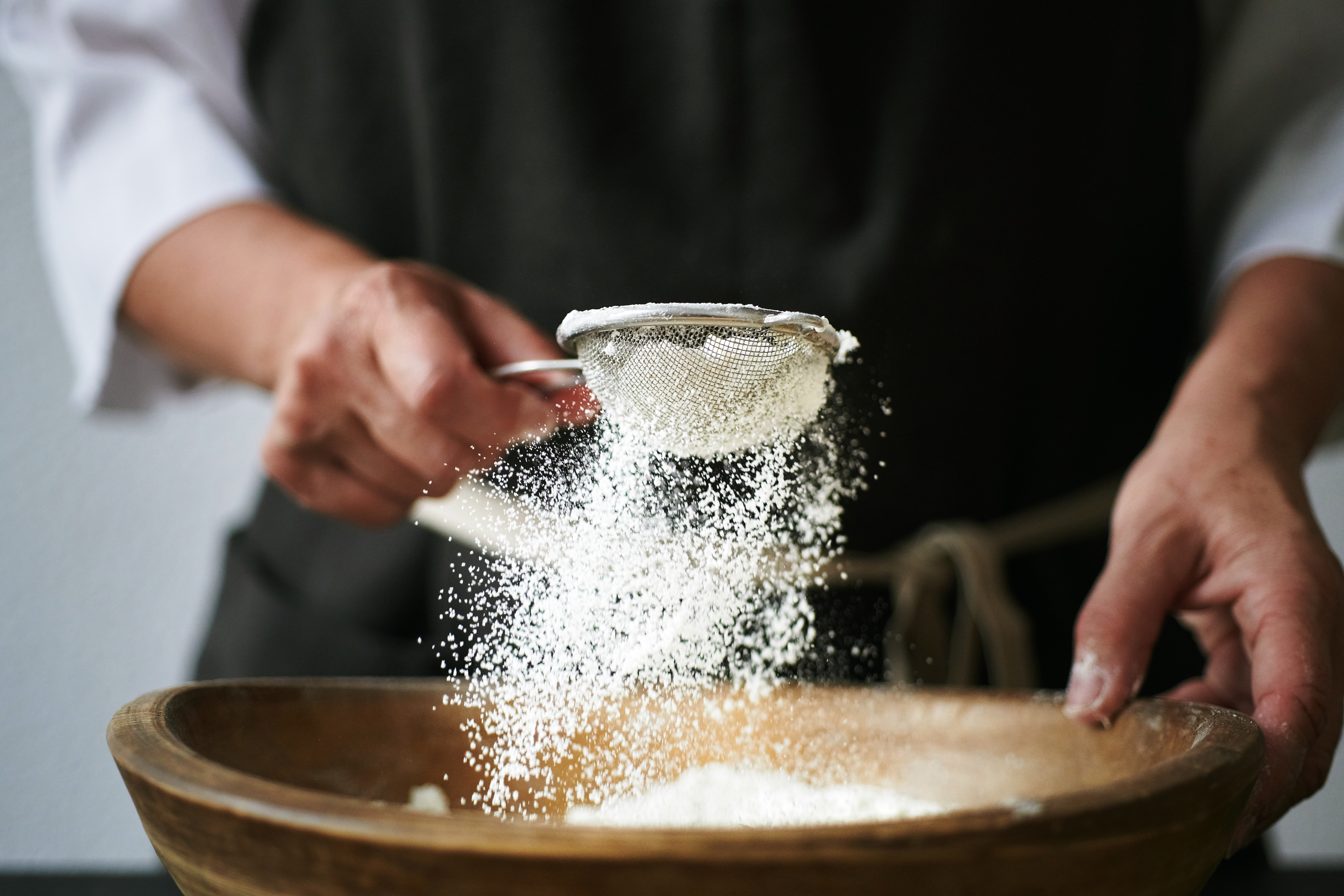 Person hands sifting flour to bowl.