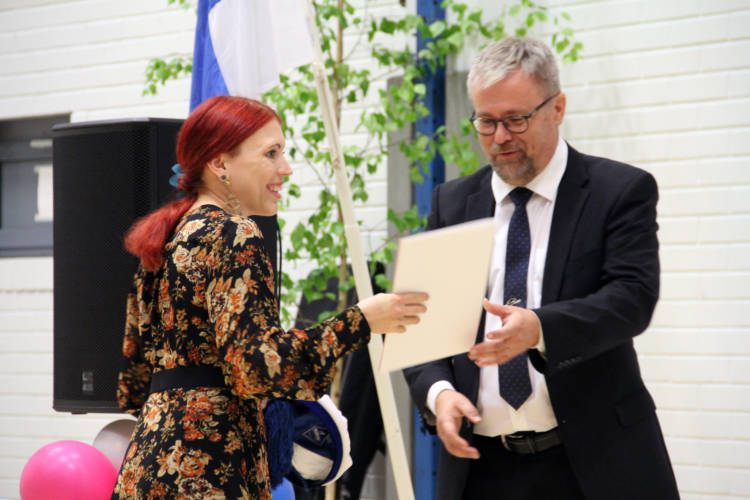 Kaksi henkilöä pitelevät todistusta. Taustalla on suomenlippu, koivu ja ilmapalloja.