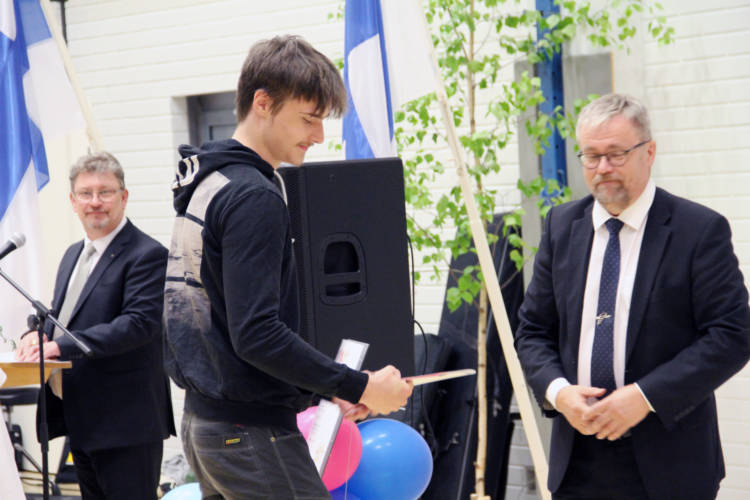 Kolme henkilöä, joista keskimmäinen pitelee todistusta.