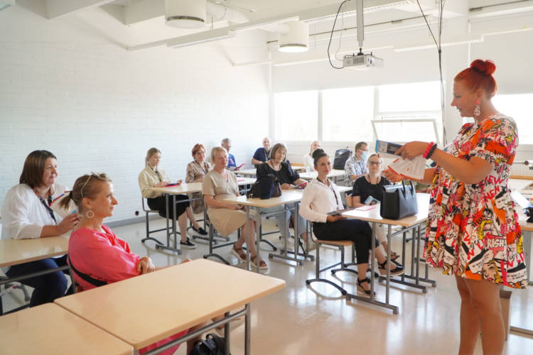 Kuvassa henkilöitä kuuntelemassa yhtä henkilöä luokkatilassa.