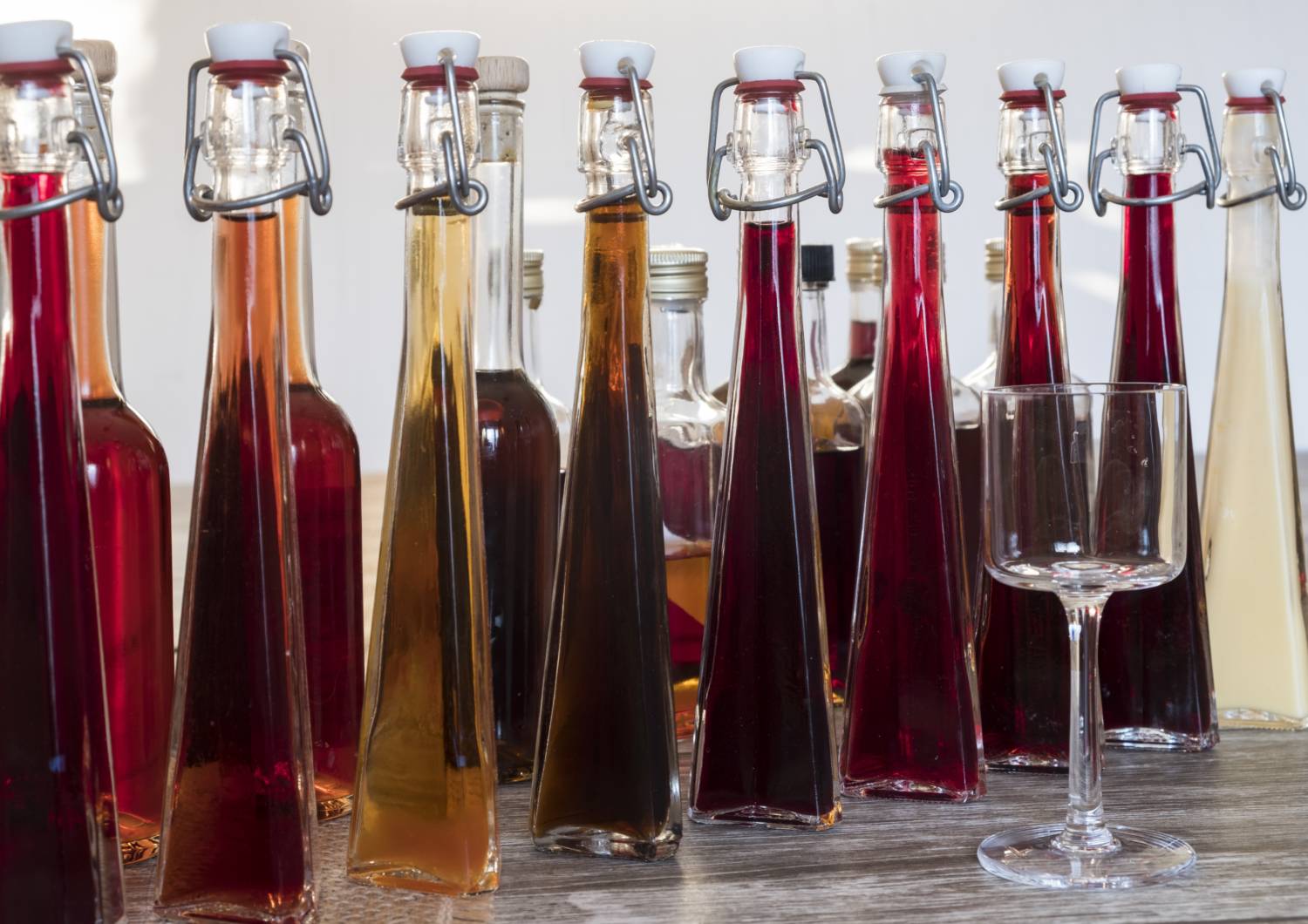 Kuvassa korkeita pulloja, jossa värikästä juomaa sekä tyhjä lasi.