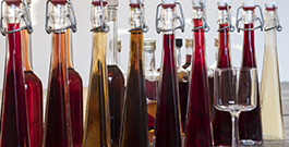 Kuvassa korkeita pulloja, jossa värikästä juomaa sekä tyhjä lasi.