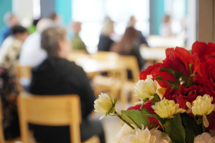 Kuvassa etualalla kukkakimppu ja takana sumeasti juhlaväkeä istumassa pöytien ääressä.