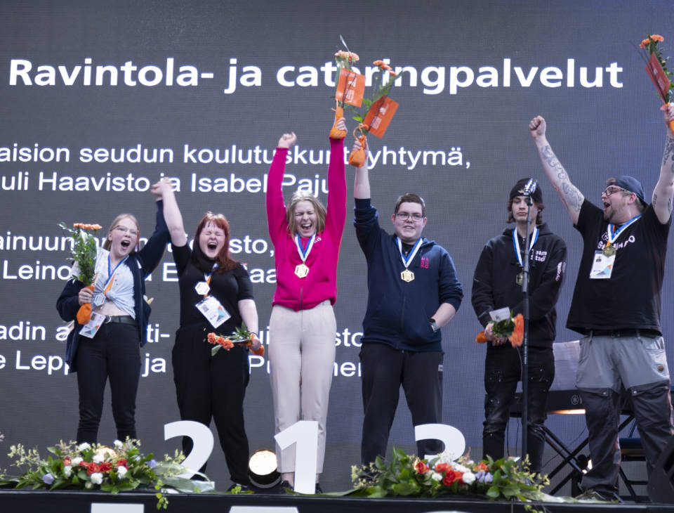 Joukko hurraavia henkilöitä palkintojenjakolavalla Taitaja-kisoissa.