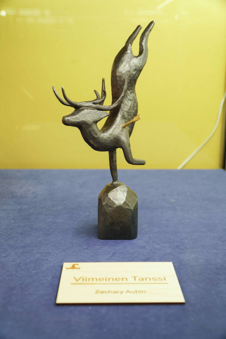 Hirvieläimen muotoinen metallinen teos. Eläimen kyljessä on puolikas metallista tehty nuoli. Vieressä kyltti, jossa lukee Viimeinen Tanssi, Zachary Aubin.