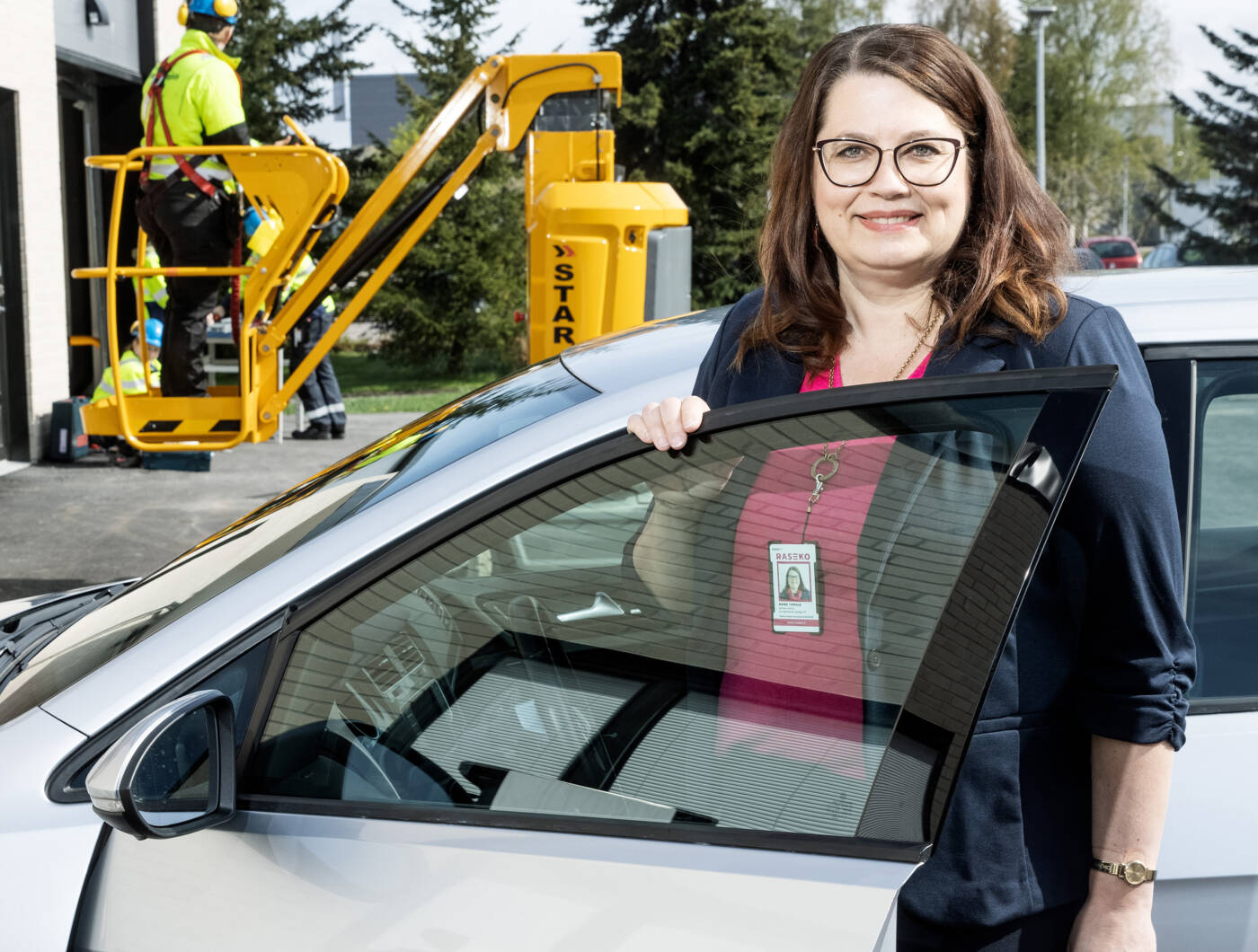 Maria taipale nousemassa autosta, takana keltaisessa nostimessa suojavarusteinen henkilö.