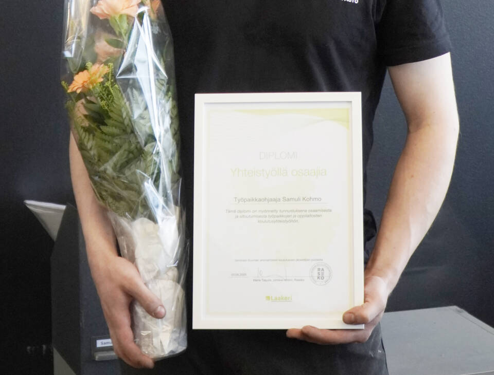 Ihmisen kädet pitelevät kukkakimppua ja kehyksissä olevaa diplomia.