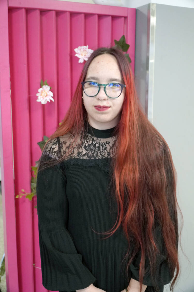 Punatukkainen nuori henkilö pinkin seinämän edessä.