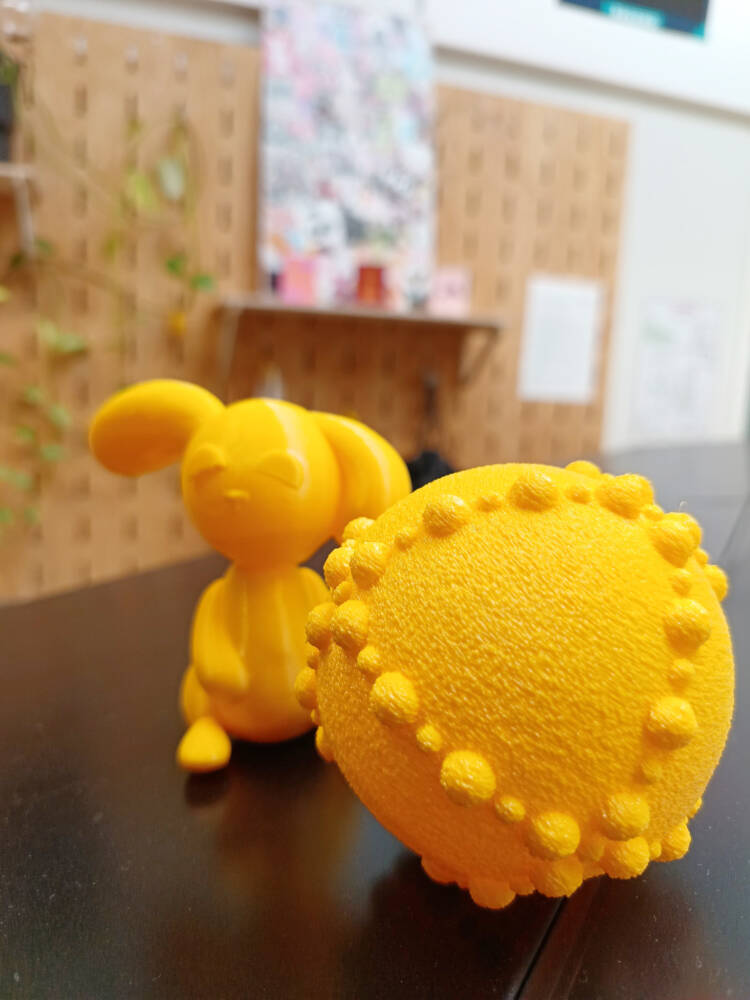 Keltainen röpöpintainen pallo ja sileäpintainen pupu, jotka on tulostettu 3D-tulostimella.