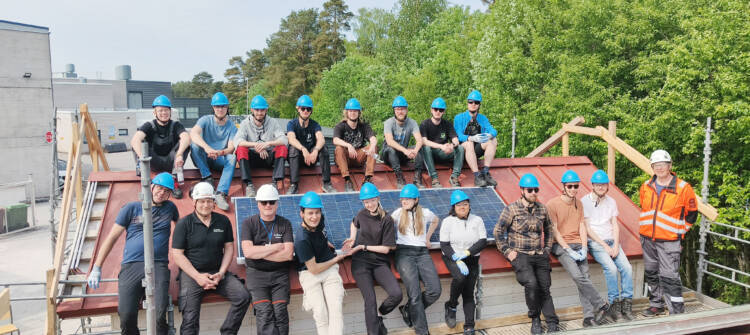 A crowd of people with helmets on sitting next to solar panels.