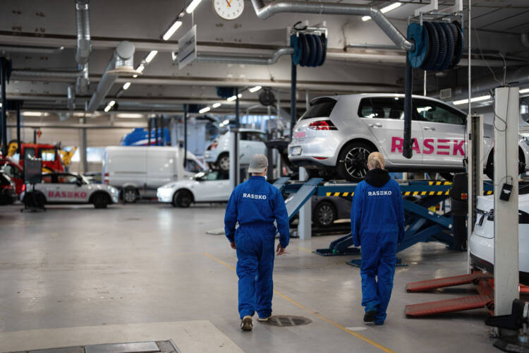 Kaksi henkilöä työhaalareissa autokorjaamossa.