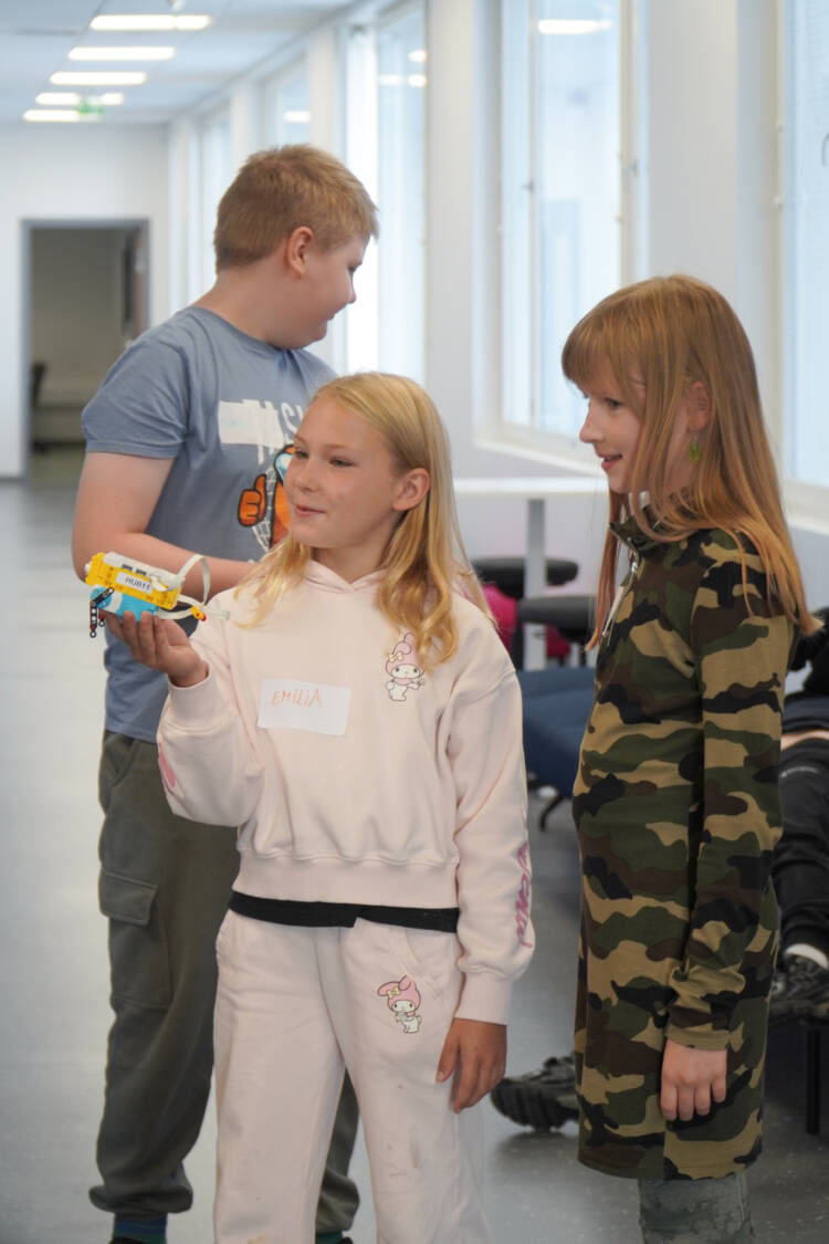 Kaksi lasta esittelee LEGO robottiaan käytävällä, toisella on robotti kädessään.
