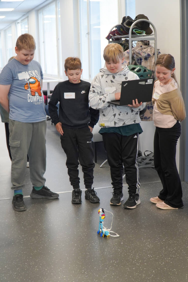 Neljä lasta esittelee robottia, joka on käytävän lattialla.