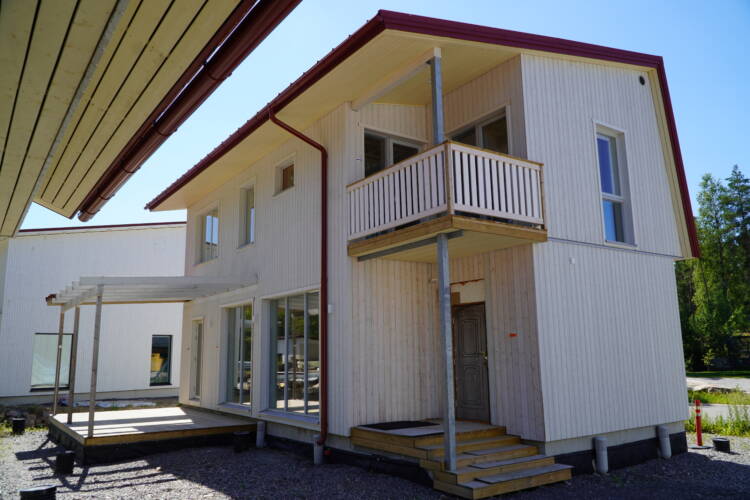 Valkoinen puuverhoiltu omakotitalo, kuvassa talon pääsisäänkäynti.