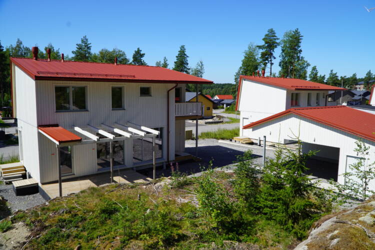 Valkoinen puuverhoiltu omakotitalo ja ulkorakennus, joissa punainen peltikatto.
