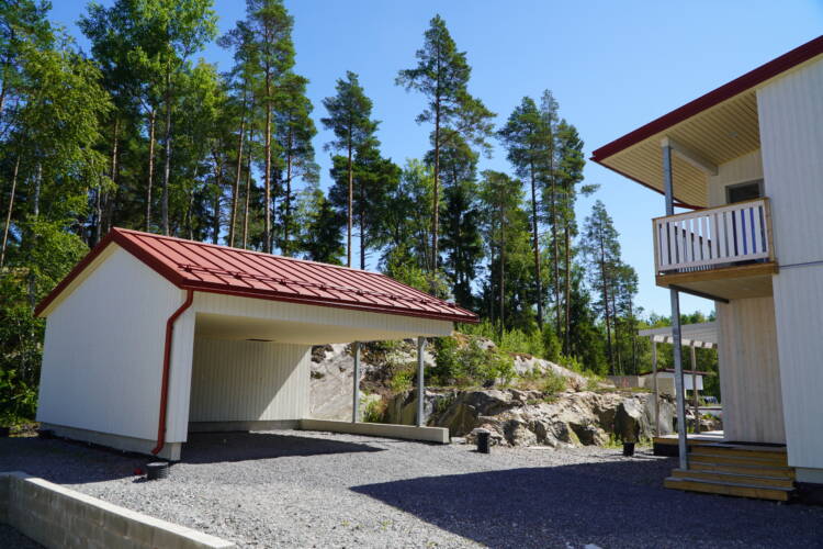 Valkoinen puuverhoiltu autokatos, jossa punainen peltikatto.